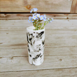 The Rustic Elegance Porcelain Mini Vase, designed in white with black patterns, holds a bunch of tiny blue flowers on a wooden surface. The Rustic Elegance Porcelain Mini Vase, designed in white with black patterns, holds a bunch of tiny blue flowers on a wooden surface.