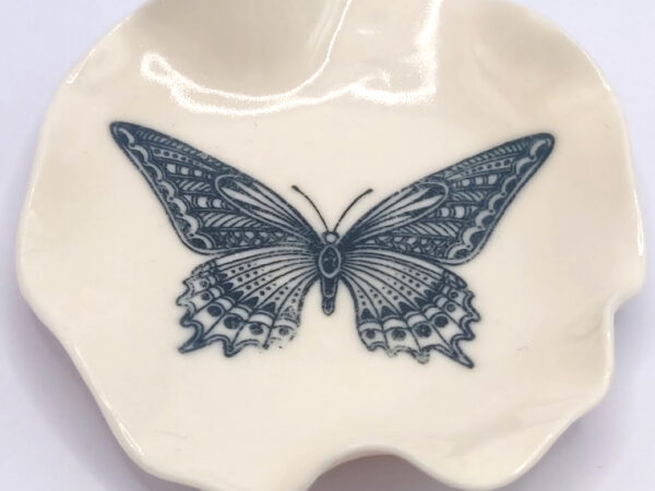 A small, cream-colored ceramic dish with a detailed black butterfly illustration at the center.