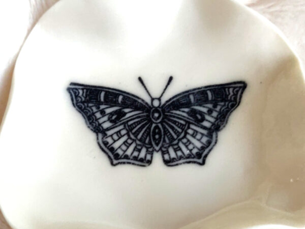 A small, white scalloped "Butterfly Ring Holder" featuring a black butterfly design (6.5 cm x 6.5 cm).