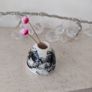 Ethereal Swirl Miniature Vase in black and white marble design with two pink dried flowers, set on a light surface adorned with clear string lights in the background.
