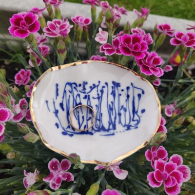 A Blue and White Porcelain Ring Holder with gold lustre is surrounded by vibrant pink flowers, showcasing its small white dish adorned with intricate blue patterns. A Blue and White Porcelain Ring Holder with gold lustre is surrounded by vibrant pink flowers, showcasing its small white dish adorned with intricate blue patterns.