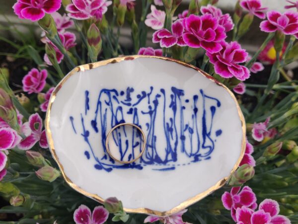 A Blue and White Porcelain Ring Holder with gold lustre is surrounded by vibrant pink flowers, showcasing its small white dish adorned with intricate blue patterns.