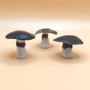 Three ceramic mushrooms with dark caps and light stems are arranged on a beige surface. Three ceramic mushrooms with dark caps and light stems are arranged on a beige surface.