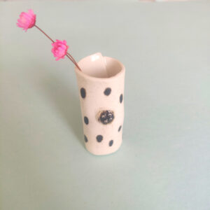 Speckled Mini Pottery Vase, featuring a black polka dot design, holding two small pink flowers, set against a light green background. Speckled Mini Pottery Vase, featuring a black polka dot design, holding two small pink flowers, set against a light green background.