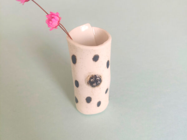 Speckled Mini Pottery Vase, featuring a black polka dot design, holding two small pink flowers, set against a light green background. Speckled Mini Pottery Vase, featuring a black polka dot design, holding two small pink flowers, set against a light green background.
